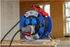 A heavy-duty extension cord reel with multiple outlets, set up on a wooden surface in what appears to be a construction or workshop environment. Anteprima dell’immagine prodotto