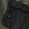 A close-up view of a black zippered pocket on olive-colored shorts. Produktbild-Vorschau