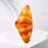 A close-up of a glazed croissant on a white surface with a shadow of leaves in the background. Podgląd zdjęcia produktu