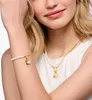 A woman wearing a white top is modeling a pearl bracelet and a gold necklace with a charm. Produktbild-Vorschau