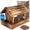 A wooden bird feeder filled with birdseed, with two small birds perched on it. A bag of birdseed and a pile of birdseed are also visible. Produktbild-Vorschau