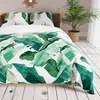 A bed with a duvet and pillows featuring a tropical leaf pattern, next to a potted plant. Podgląd zdjęcia produktu