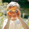 A young boy is looking through yellow binoculars outdoors. Produktbild-Vorschau