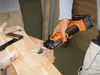 A person is using a cordless oscillating multi-tool to cut into a wooden plank. Náhľad obrázku produktu