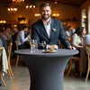 A man in a suit stands behind a round table at an event. Produktbild-Vorschau