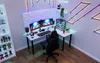 A modern gaming setup with a corner desk, multiple monitors, and LED lighting. Anteprima dell’immagine prodotto