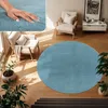 A circular blue rug is placed on a wooden floor in a living room setting, with a chair and plants nearby. Produktbild-Vorschau