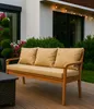A beige outdoor sofa with cushions is placed on a wooden deck, surrounded by greenery and flowers. String lights are visible in the background. Produktbild-Vorschau
