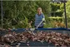 A woman is using a leaf blower on a trampoline covered in leaves. Produktbild-Vorschau