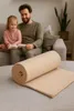 A father and daughter are sitting on a couch reading a book, with a rolled-up blanket in the foreground. Produktbild-Vorschau