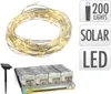A coiled string of solar-powered LED lights and a solar panel stake, with packaging in the background. Podgląd zdjęcia produktu