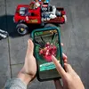 A person is holding a smartphone displaying an augmented reality game, with a LEGO stunt truck in the background. Náhľad obrázku produktu
