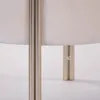 A close-up view of the base of a lamp or stool, showing metallic legs and a fabric shade. Podgląd zdjęcia produktu