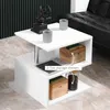 A white S-shaped side table with storage compartments, placed in a living room setting next to a black sofa. Decorative items like a coffee grinder, cups, boxes, and a jar are placed on and inside the table. Produktbild-Vorschau