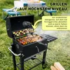 A charcoal grill is set up outdoors on a grassy area, with food cooking on the grates and a table and chairs visible in the background. Podgląd zdjęcia produktu