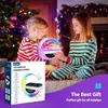 Two young girls in pajamas are looking at a colorful LED wireless charging speaker with a clock display, with a Christmas tree in the background. Produktbild-Vorschau