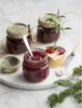 Three jars of jam are arranged on a marble surface, with a slice of bread topped with cheese and jam, and a sprig of rosemary. A pine branch is in the foreground. Produktbild-Vorschau