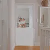A woman holds a baby while standing in a doorway with a white baby gate installed. Voir les images du produit
