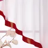 A close-up of a sheer white curtain with a red satin ribbon trim. Produktbild-Vorschau
