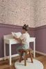 A young girl sits at a white desk reading a book in a room with floral wallpaper and purple wainscoting. Náhled obrázku produktu