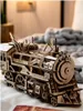A detailed wooden model of a steam locomotive is displayed on a surface, with a blurred background of a room. Náhľad obrázku produktu