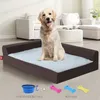 A golden retriever dog sits on a brown dog bed with a light blue fluffy insert. In the foreground, a blue portable drinking bowl and three bone-shaped chew toys (pink, blue, and yellow) are displayed with text labels. Náhled obrázku produktu