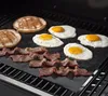 Breakfast items like pancakes, fried eggs, and bacon are being cooked on a grill mat on a barbecue grill. Produktbild-Vorschau