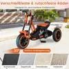 An orange and black children's tricycle is shown outdoors on a paved surface, with various road surfaces illustrated below. Produktbild-Vorschau