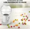 A white candy dispenser is shown on a white surface with colorful candies scattered around it. The background is blurred. Anteprima dell’immagine prodotto