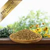 A wooden bowl filled with seeds sits on a wooden surface, with a blurred background of green foliage and yellow flowers. A golden ribbon with the word "PREMIUM" is in the top left corner. Produktbild-Vorschau