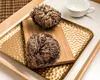 Two dried plants, resembling dried flowers or moss balls, are displayed on a wooden board placed on a textured gold tray. A white teacup is visible in the background. Voir les images du produit