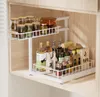 A two-tier pull-out kitchen organizer filled with various bottles and jars, placed on a shelf inside a cabinet. Voir les images du produit