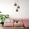 A modern living room scene with a pink sectional sofa, a large potted plant, and a small side table with plants and books. Three pendant lights hang above. Náhľad obrázku produktu