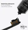 A tube of black toothpaste is squeezing toothpaste onto a black toothbrush with orange bristles. The background is white. Produktbild-Vorschau