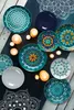 A collection of decorative plates with mandala patterns, arranged on a dark surface with candles. Anteprima dell’immagine prodotto