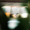 Three clear plastic storage containers with beige lids are arranged on a shelf, illuminated by strip lights below. Produktbild-Vorschau