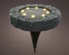 A solar-powered ground light with a stone-like texture and illuminated LEDs. Produktbild-Vorschau