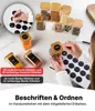 Hände schreiben auf und bringen schwarze Etiketten auf klaren Gewürzgläsern mit Bambusdeckeln an, gefüllt mit verschiedenen Gewürzen Anteprima dell’immagine prodotto