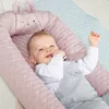 A baby is lying in a pink baby lounger with bunny ears on a light blue mat. Produktbild-Vorschau