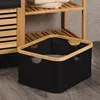 A black storage basket with a bamboo frame sits on a wooden floor next to a wooden shelf unit. Anteprima dell’immagine prodotto