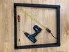 A black metal table frame is laid out on a wooden floor, along with a screwdriver, a cordless drill, and a measuring tape. Anteprima dell’immagine prodotto