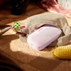 A pink Bose SoundLink Flex speaker is partially inside a beige textured bag, surrounded by makeup, a hairbrush, and shoes. Produktbild-Vorschau