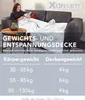 A woman is relaxing on a couch under a weighted blanket, reading a magazine. A coffee table with a lamp and teapot is beside her. Produktbild-Vorschau