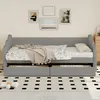 A gray daybed with bedding, a blanket, and pillows, set in a room with artwork on the wall and a rug on the floor. Produktbild-Vorschau