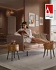 A woman sits on a couch reading a book, with decorative stools in the foreground and artwork on the wall. Náhled obrázku produktu