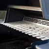 Close-up view of a stainless steel warming rack with a drumstick holder, inside a grill. Podgląd zdjęcia produktu