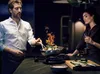 A man is cooking with a wok on a stove, with a woman watching and holding a glass of wine. Anteprima dell’immagine prodotto