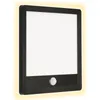 A black LED outdoor wall lamp with a motion sensor is shown against a white background. A soft yellow glow emanates from the sides of the lamp. Produktbild-Vorschau