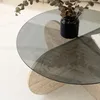 A close-up of a round glass coffee table with a travertine base, featuring a vase with dried eucalyptus. Produktbild-Vorschau