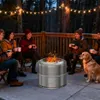 People and a dog gathered around a bonfire on a deck at dusk. Produktbild-Vorschau